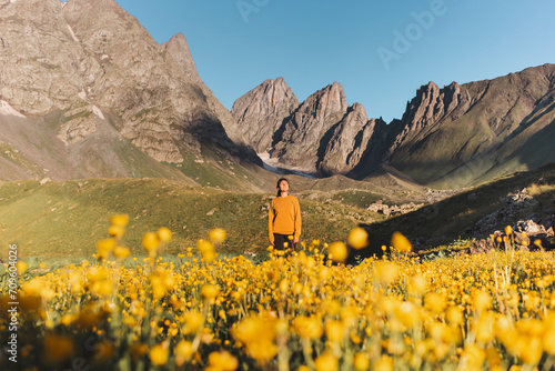 Young woman standing near yellow flowers in front of Caucasus mountains photo