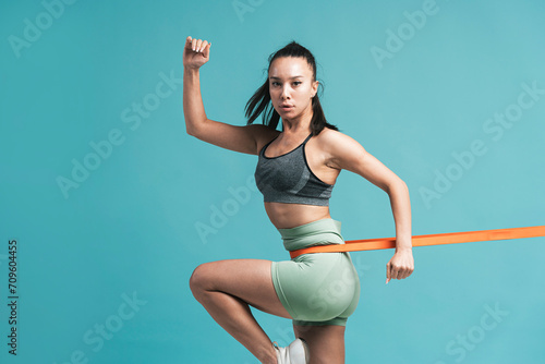 Confident young woman exercising with resistance band against blue background photo