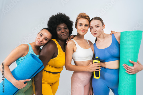 Confident multiracial female friends with yoga mats and water bottle against white background photo