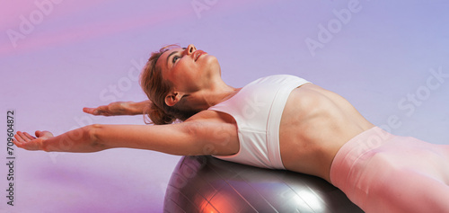 Woman exercising on fitness ball with arms stretched against two tone background photo