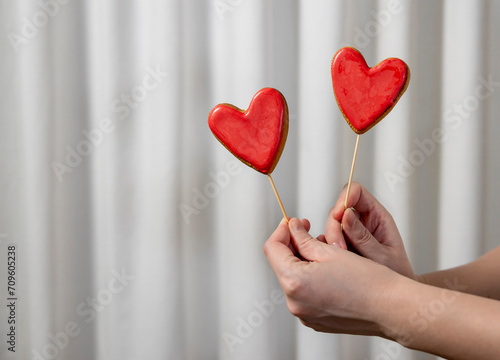 Hands of woman holding red heart shaped cookies in front of white curtain photo