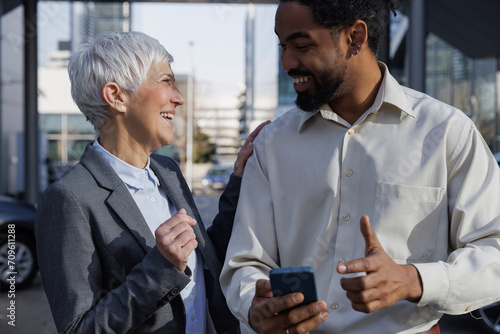 Happy businesswoman with hand on shoulder of colleague holding smart phone photo
