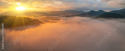 Amazing morning fog in the mountains. Beautiful sunrise light shines on the red beech forest. Drone panorama. © Ryzhkov Oleksandr