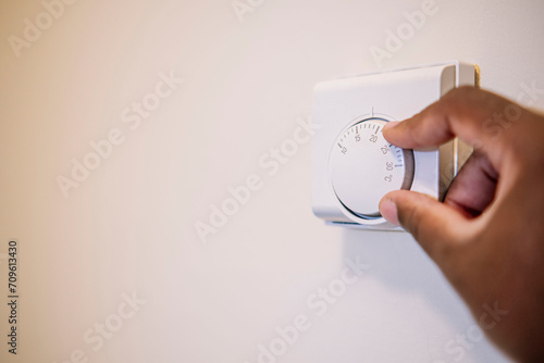 Hand of man adjusting temperature of thermostat at home photo