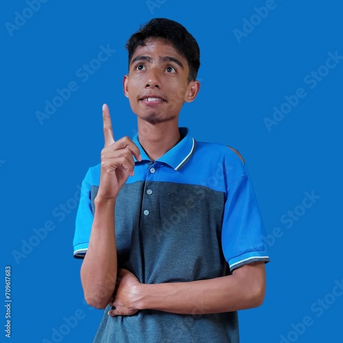 young asian smiling finger pointing to empty space, isolated blue background