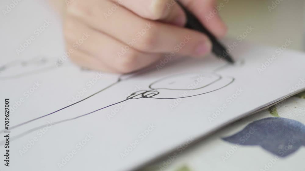 Closeup of a kid's hand doodling on a white paper with a black marker. Closeup of a kid's hand doodling on a white paper with a black marker.