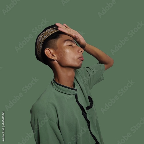 Confused young Asian muslim man Holding head with both hands, isolated green background.