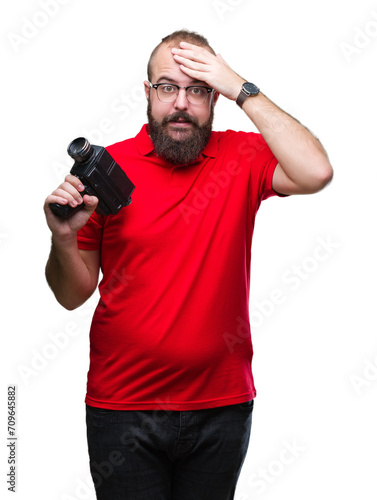 Young caucasian hipster man filmming using retro video camera over isolated background stressed with hand on head, shocked with shame and surprise face, angry and frustrated