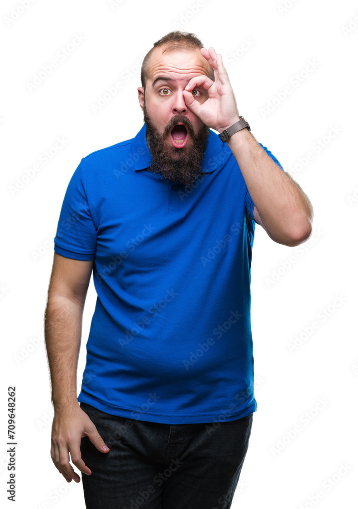 Young caucasian hipster man wearing blue shirt over isolated background doing ok gesture shocked with surprised face, eye looking through fingers. Unbelieving expression. Young caucasian hipster man wearing blue shirt over isolated background doing ok gesture shocked with surprised face, eye looking through fingers. Unbelieving expression.