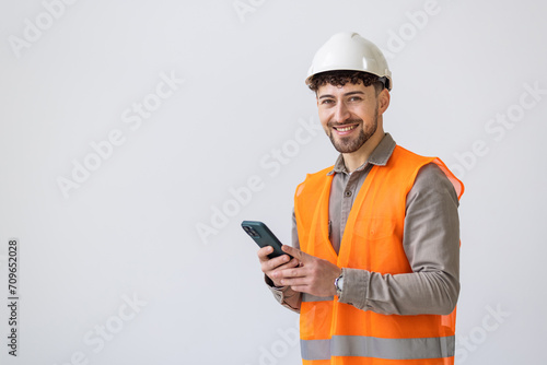 Young man worker or builder in yellow helmet and overall with smartphone over white background