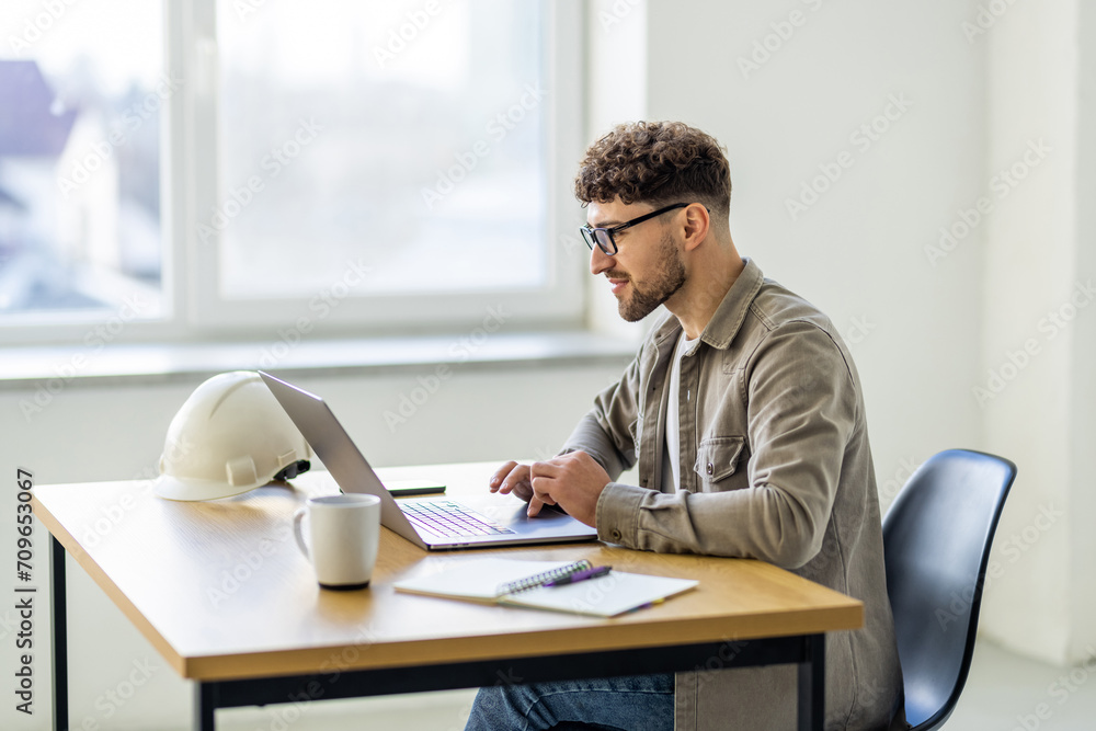 Young man working at home with laptop and papers on desk