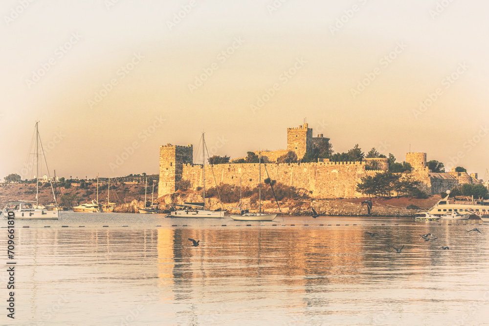 Panoramic view to the Bodrum Castle reflecting at waters of harbor at sunrise, flock of birds fluing under calm water. Old postcard stylization. Bodrum (Mugla), Turkey