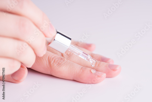 Pipette with a colorless drop of anti-brittle nails or oil for cuticles. The woman cares for hands and nails, close up. Woman applying oil to cuticle. Healthy nails concept, massage.