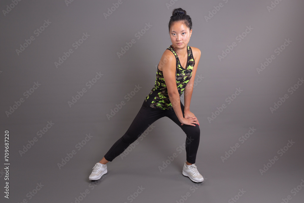 Asian athlete in camo tank and leggings performs a side stretch