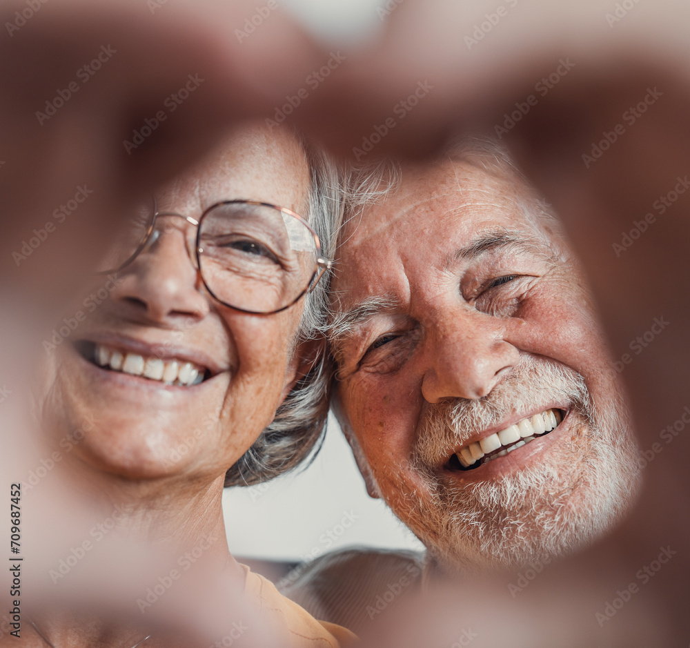 Close up portrait happy sincere middle aged elderly retired family couple making heart gesture with fingers, showing love or demonstrating sincere feelings together indoors, looking at camera.. Close up portrait happy sincere middle aged elderly retired family couple making heart gesture with fingers, showing love or demonstrating sincere feelings together indoors, looking at camera..