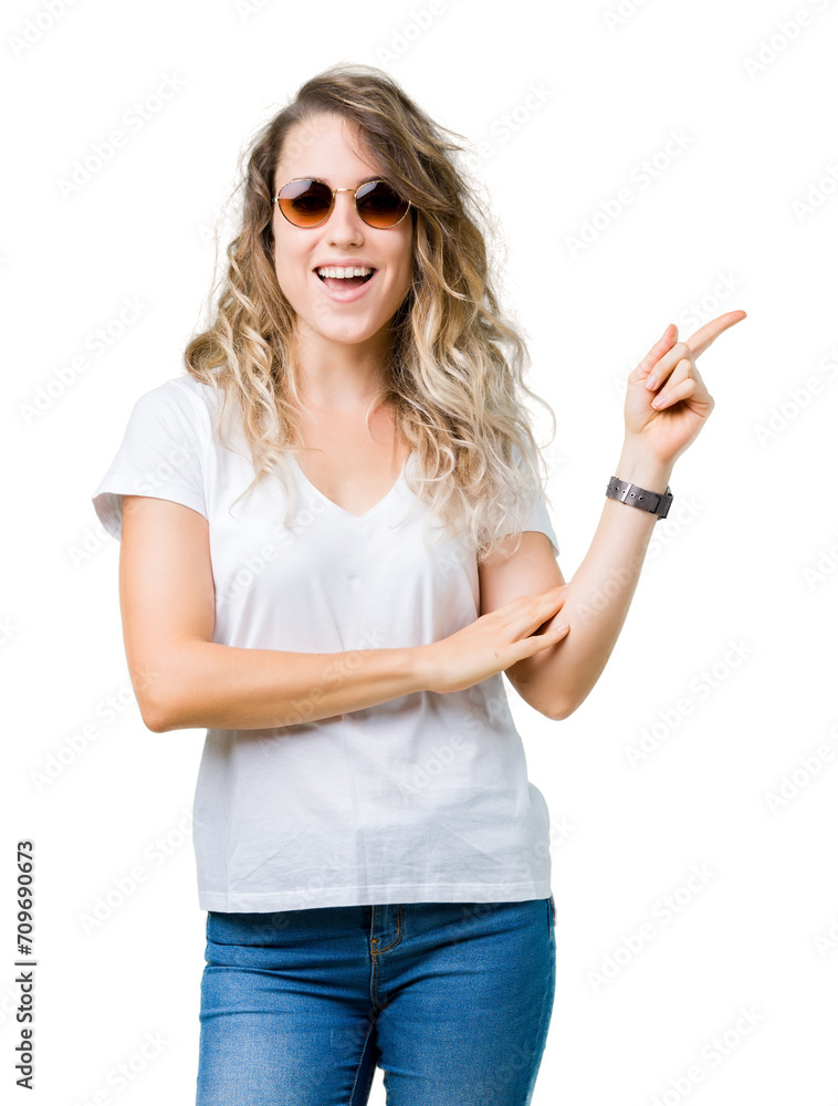 Beautiful young blonde woman wearing sunglasses over isolated background with a big smile on face, pointing with hand and finger to the side looking at the camera. Beautiful young blonde woman wearing sunglasses over isolated background with a big smile on face, pointing with hand and finger to the side looking at the camera.