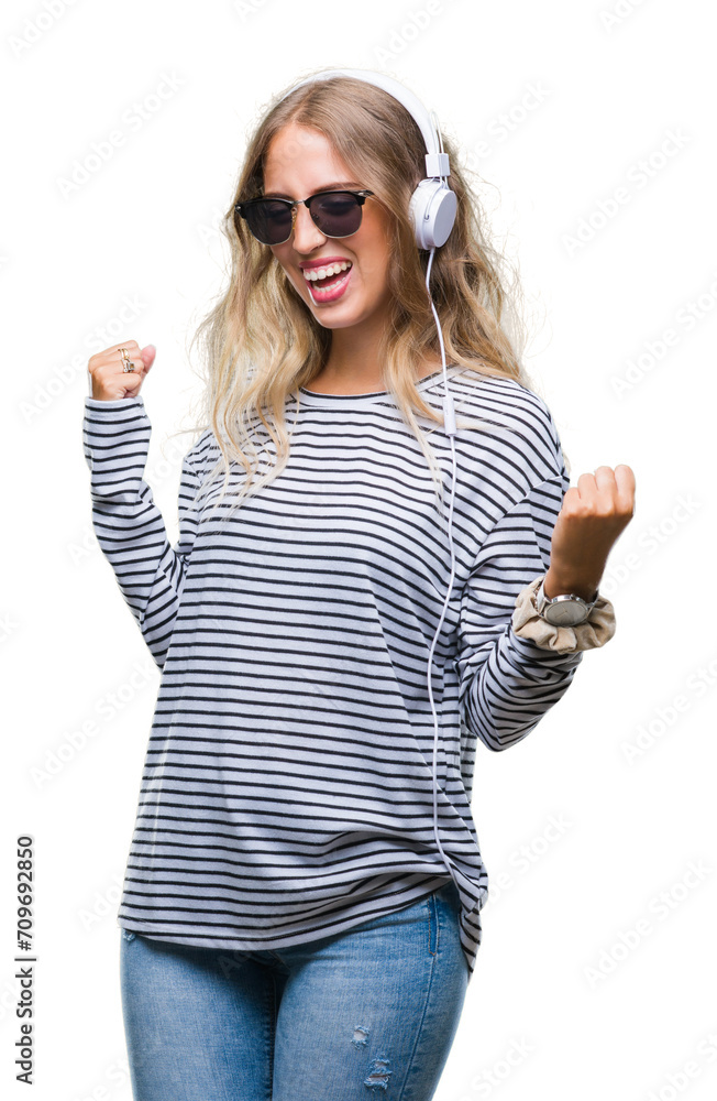 Beautiful young blonde woman wearing headphones and sunglasses over isolated background very happy and excited doing winner gesture with arms raised, smiling and screaming for success Beautiful young blonde woman wearing headphones and sunglasses over isolated background very happy and excited doing winner gesture with arms raised, smiling and screaming for success