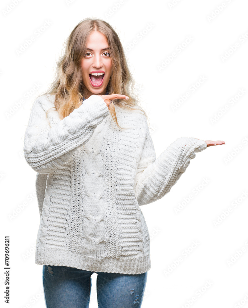 Beautiful young blonde woman wearing winter sweater over isolated background amazed and smiling to the camera while presenting with hand and pointing with finger. Beautiful young blonde woman wearing winter sweater over isolated background amazed and smiling to the camera while presenting with hand and pointing with finger.