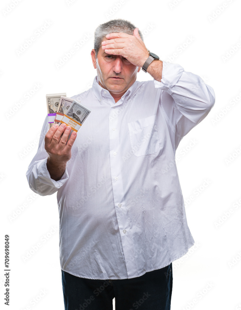 Handsome senior man holding bunch of money over isolated background stressed with hand on head, shocked with shame and surprise face, angry and frustrated. Fear and upset for mistake. Handsome senior man holding bunch of money over isolated background stressed with hand on head, shocked with shame and surprise face, angry and frustrated. Fear and upset for mistake.