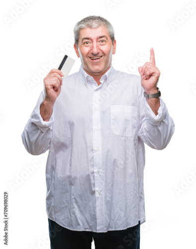 Handsome senior man holding credit card over isolated background surprised with an idea or question pointing finger with happy face, number one