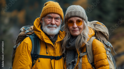 Travel concept. Winter time. Mature woman and man dressed in yellow jackets, knitted hats, with rucksacks are going to hike. Selective focus
