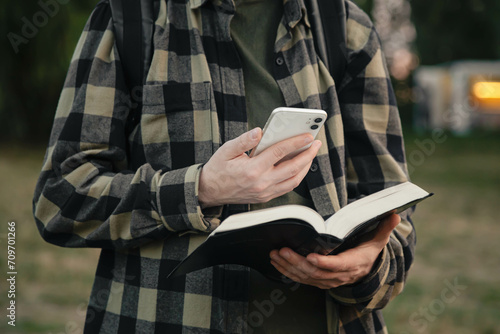 A man with a smartphone and a Bible in his hands outside, christian online technology concept, online live church, Holy Bible book and online study. photo