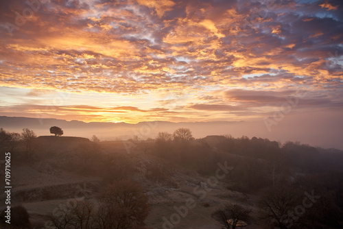 Sunrise with a landscape of a foggy field with the sky full of red clouds