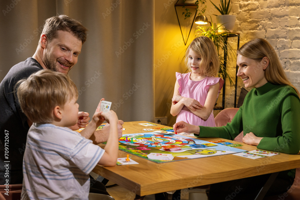 Obraz premium family with two children spending time together and and playing board games while sitting by the table at home. bonding activities