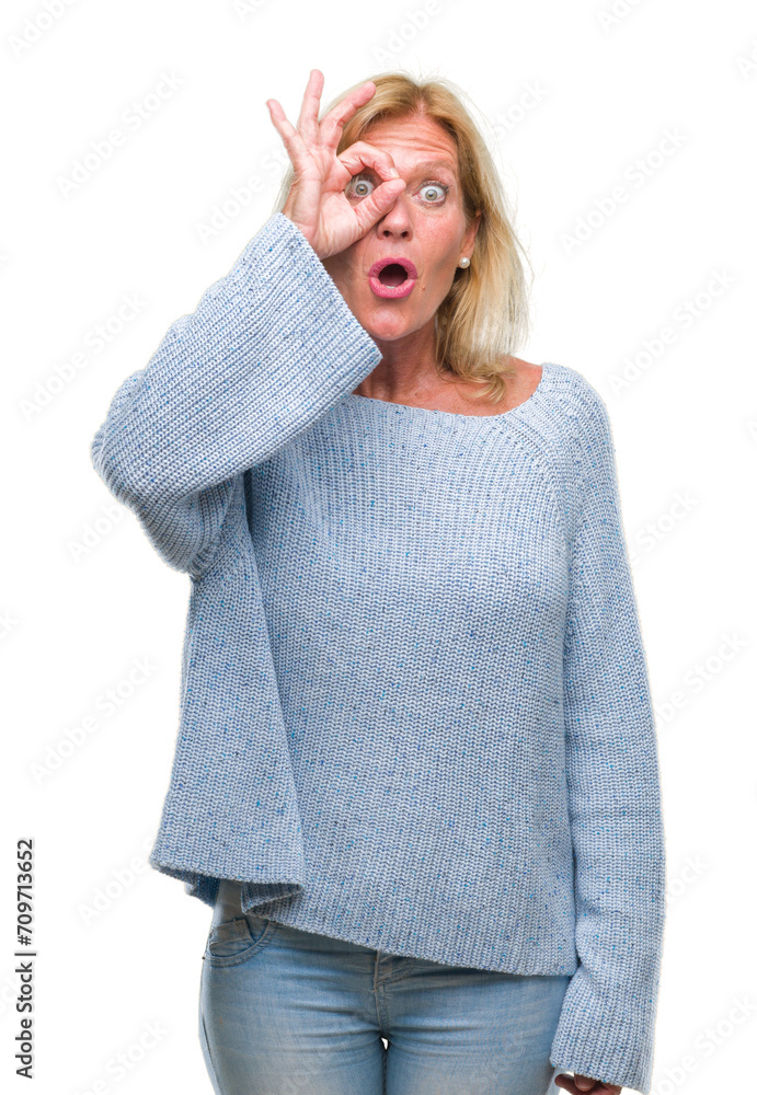 Middle age blonde woman wearing winter sweater over isolated background doing ok gesture shocked with surprised face, eye looking through fingers. Unbelieving expression. Middle age blonde woman wearing winter sweater over isolated background doing ok gesture shocked with surprised face, eye looking through fingers. Unbelieving expression.