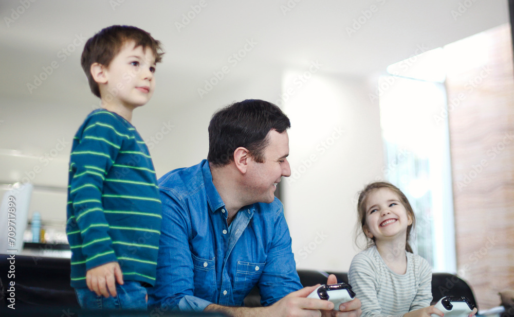 Smiling young man playing videogame together with son and daughter in modern living room Smiling young man playing videogame together with son and daughter in modern living room