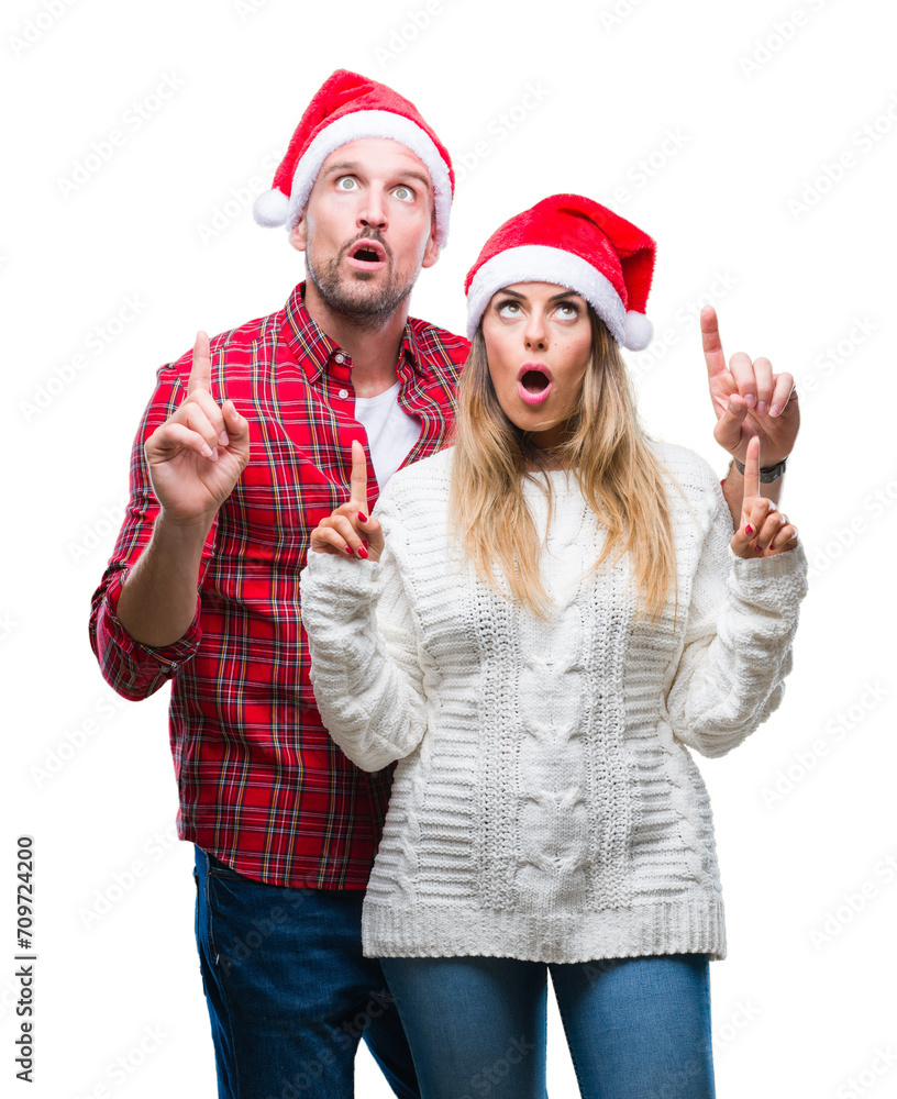 Young couple in love wearing christmas hat over isolated background amazed and surprised looking up and pointing with fingers and raised arms. Young couple in love wearing christmas hat over isolated background amazed and surprised looking up and pointing with fingers and raised arms.