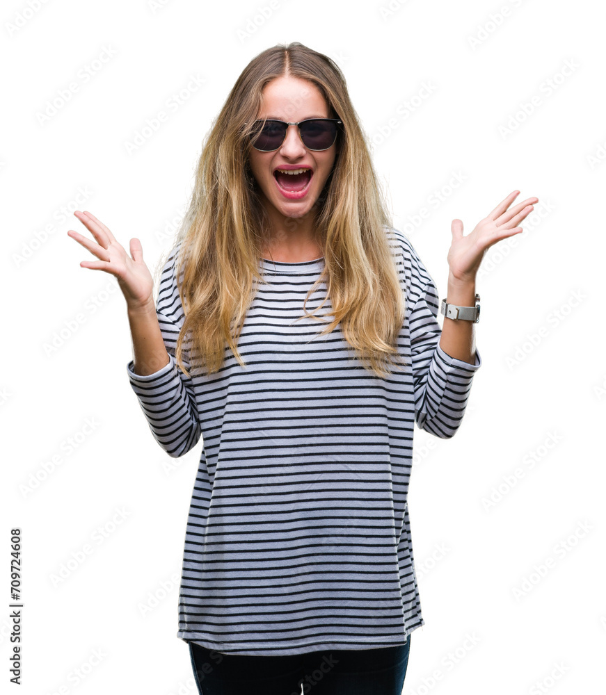 Young beautiful blonde woman wearing sunglasses over isolated background celebrating crazy and amazed for success with arms raised and open eyes screaming excited. Winner concept Young beautiful blonde woman wearing sunglasses over isolated background celebrating crazy and amazed for success with arms raised and open eyes screaming excited. Winner concept