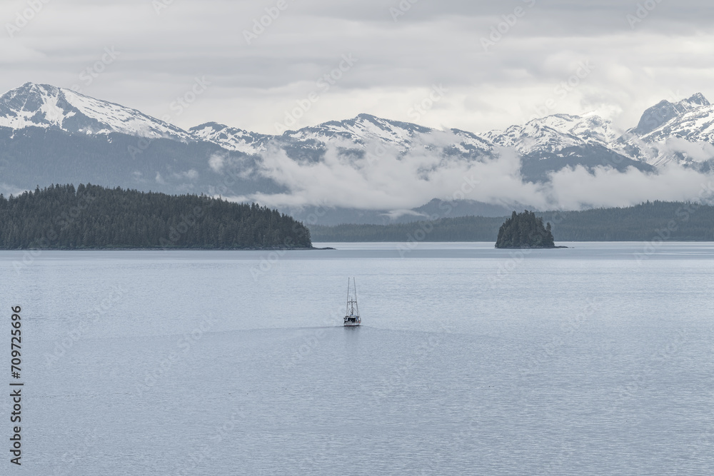 Commercial fishing boat  in Sitka sound with clouds around the mountains beyond, Alaska, USA