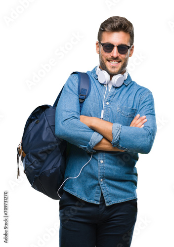 Young handsome tourist man wearing headphones and backpack over isolated background happy face smiling with crossed arms looking at the camera. Positive person. © Krakenimages.com