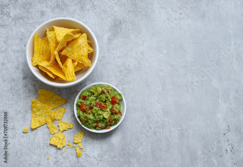 Top view of tortilla chips in a white bowl and avocado guacamole on grey table  photo