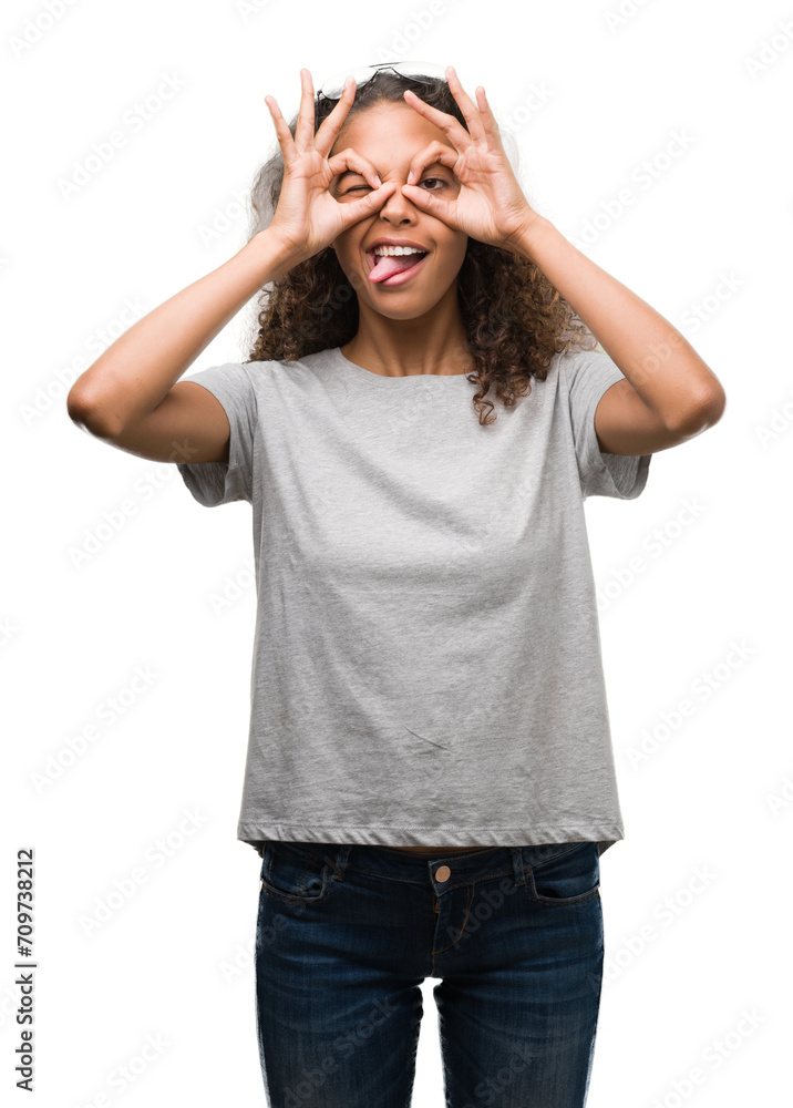 Beautiful young hispanic woman wearing glasses doing ok gesture like binoculars sticking tongue out, eyes looking through fingers. Crazy expression. Beautiful young hispanic woman wearing glasses doing ok gesture like binoculars sticking tongue out, eyes looking through fingers. Crazy expression.