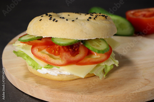 Delicious bagel with vegan cheese, fresh vegetables on wooden plate