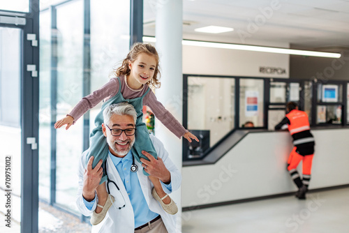 Portrait of a pediatrician with a little patient sitting on his shoulders, piggyback. Friendly relationship between the doctor and the child patient.