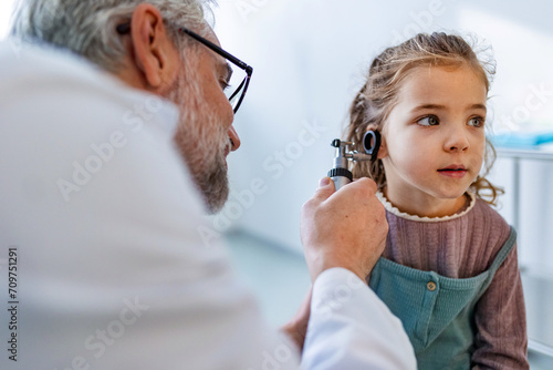 Doctor examining little girl's ear using otoscope, looking for infection. Friendly relationship between the doctor and the child patient. photo