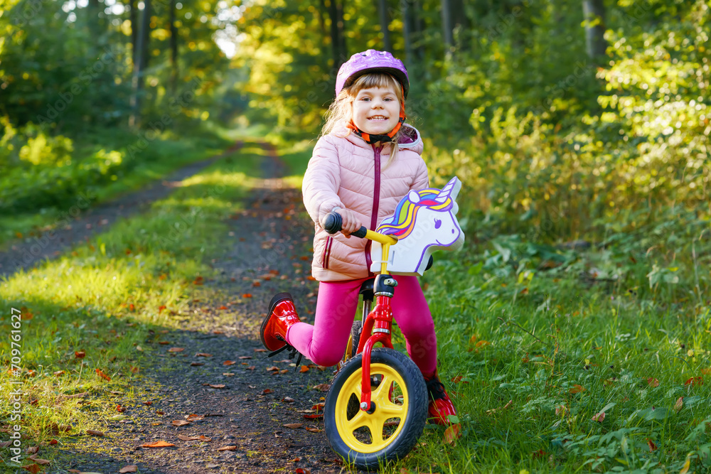 Child riding balance bike. Kids on bicycle in sunny forest. Little girl enjoying to ride glider bike on warm day. Preschooler learning to balance on run bicycle in safe helmet. Sport activity Child riding balance bike. Kids on bicycle in sunny forest. Little girl enjoying to ride glider bike on warm day. Preschooler learning to balance on run bicycle in safe helmet. Sport activity