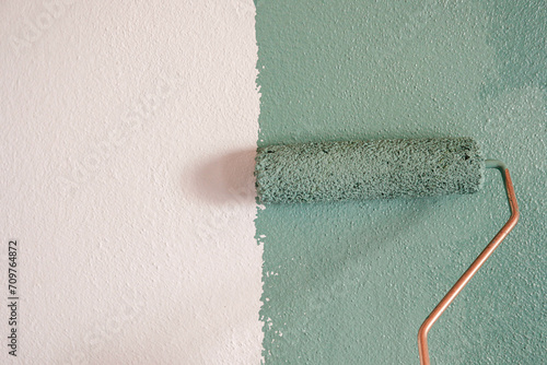 Repairman painting white wall in apartment green using roller, closeup photo