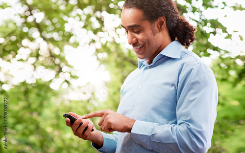 Handsome dark skin man dialin a number on the smartphone in the park photo