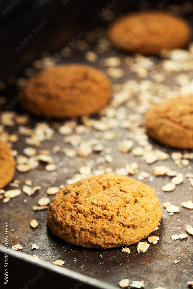 Craft and rustic four oatmeal cookies. Dark food aesthetics, black background with several oat flakes. Craft and rustic four oatmeal cookies. Dark food aesthetics, black background with several oat flakes.