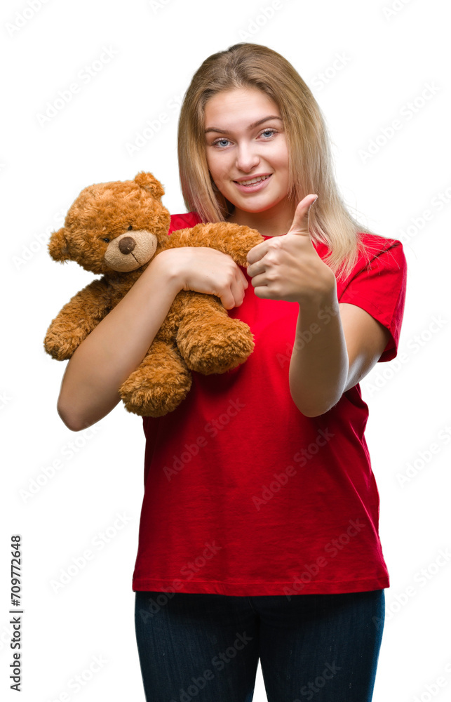 Young caucasian woman holding cute teddy bear over isolated background happy with big smile doing ok sign, thumb up with fingers, excellent sign Young caucasian woman holding cute teddy bear over isolated background happy with big smile doing ok sign, thumb up with fingers, excellent sign