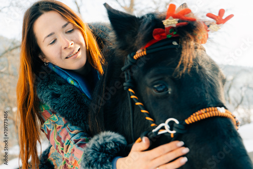 Woman bareback on beautiful black horse outdoors in winter. Decorative bridle and Christmas decorations on horse's head