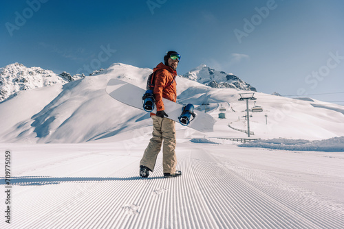 snowboarder holding snowboard walking along ski slope at  resort prepared by snowcat