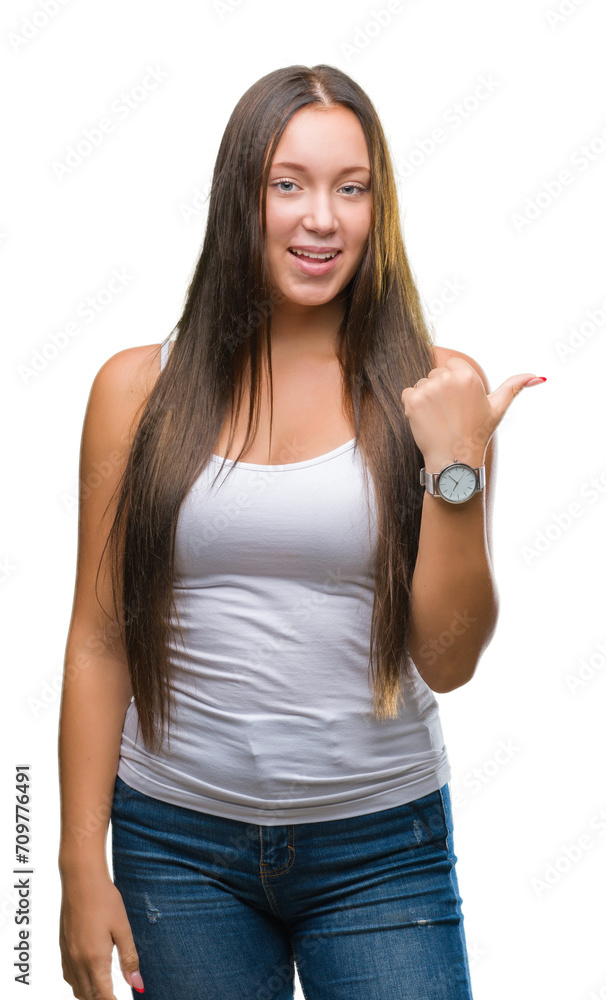 Young caucasian beautiful woman over isolated background smiling with happy face looking and pointing to the side with thumb up. Young caucasian beautiful woman over isolated background smiling with happy face looking and pointing to the side with thumb up.