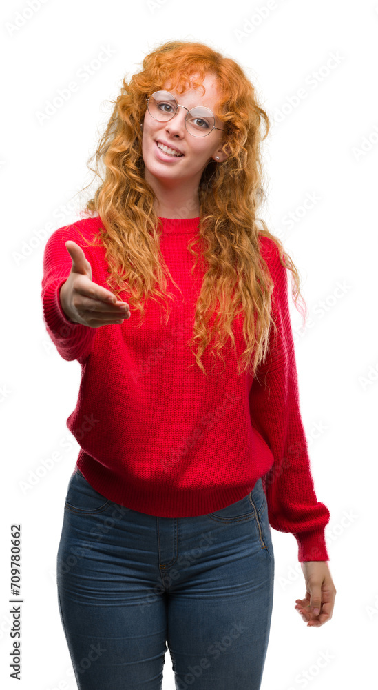 Young redhead woman wearing red sweater smiling friendly offering handshake as greeting and welcoming. Successful business.