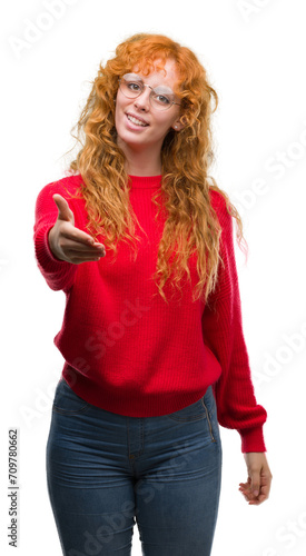 Young redhead woman wearing red sweater smiling friendly offering handshake as greeting and welcoming. Successful business. © Krakenimages.com