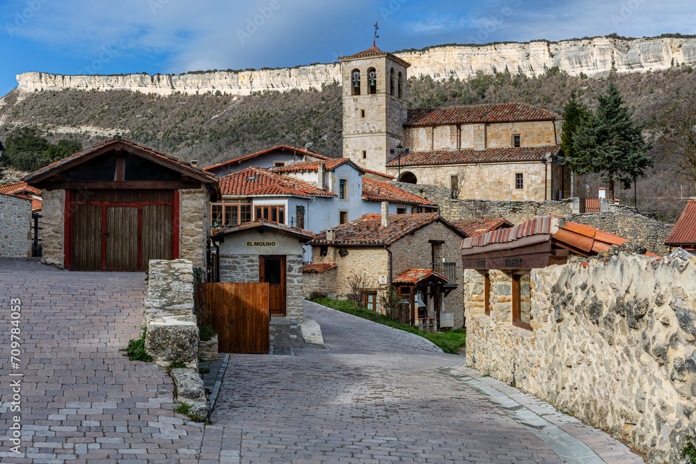 Fototapeta premium Puentedey town, houses, Church of San Pelayo and vertical rock walls in the background. Burgos, Castilla y León, Spain.